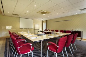 A conference room with a long table, red chairs, a projector screen, and a whiteboard.