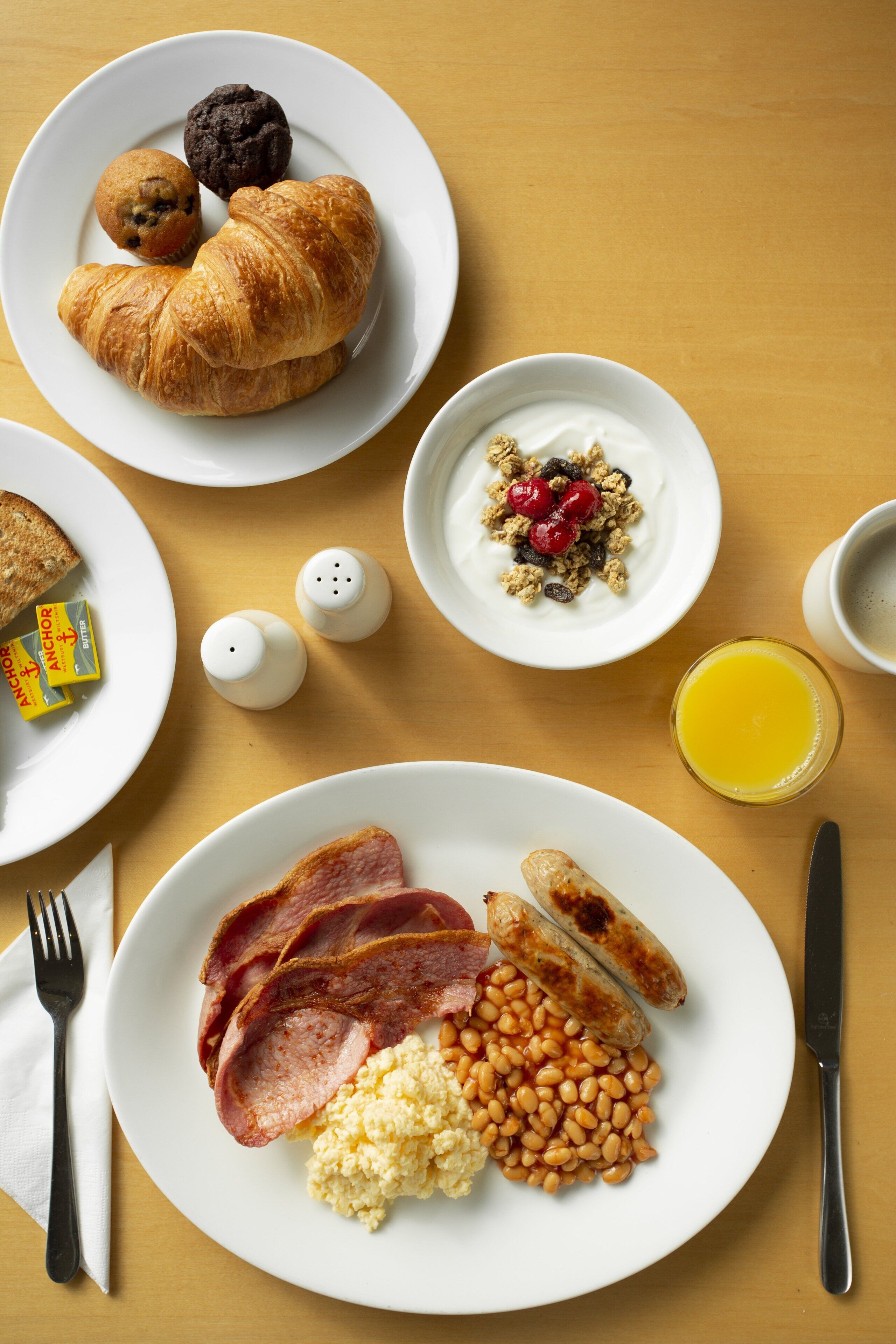 Una mesa de desayuno con platos de comida, incluyendo huevos, salchichas y productos de panadería.