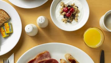 Una mesa de desayuno con platos de comida, incluyendo huevos, salchichas y productos de panadería.
