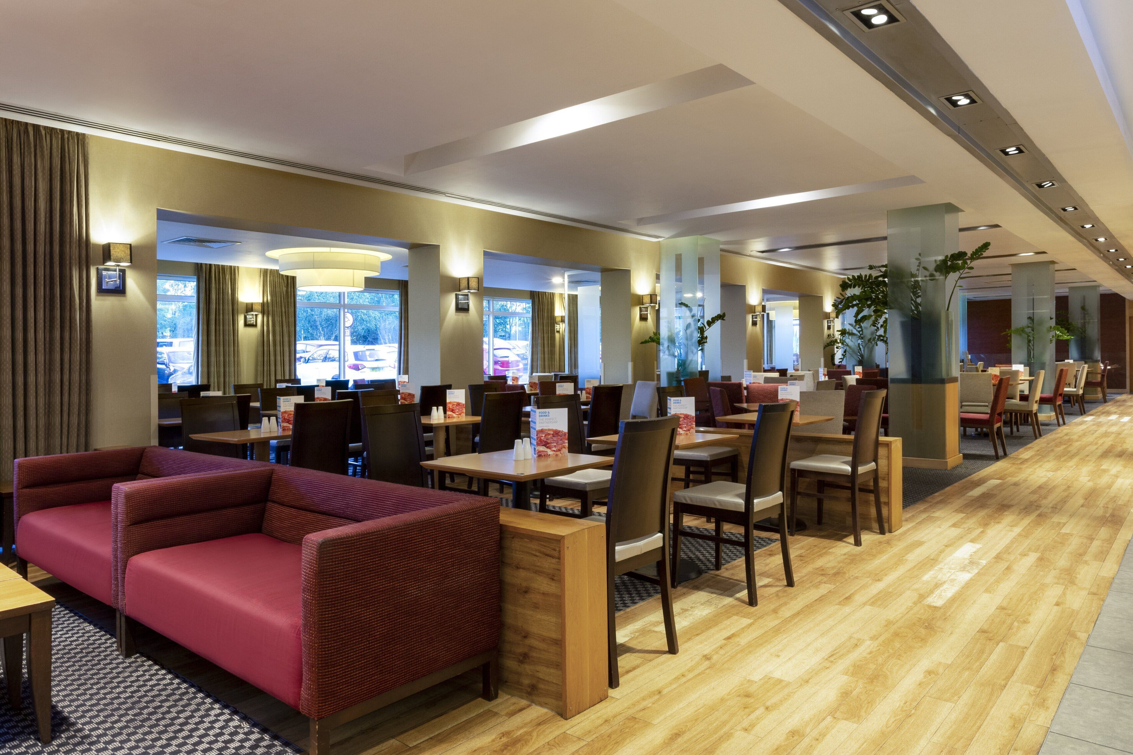 A hotel lobby with seating areas, tables, and a view of the parking lot.