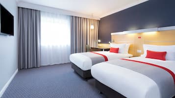 Ein Hotelzimmer mit zwei Betten, einem Fernseher, einem Schreibtisch und einem Fenster mit Vorhängen.