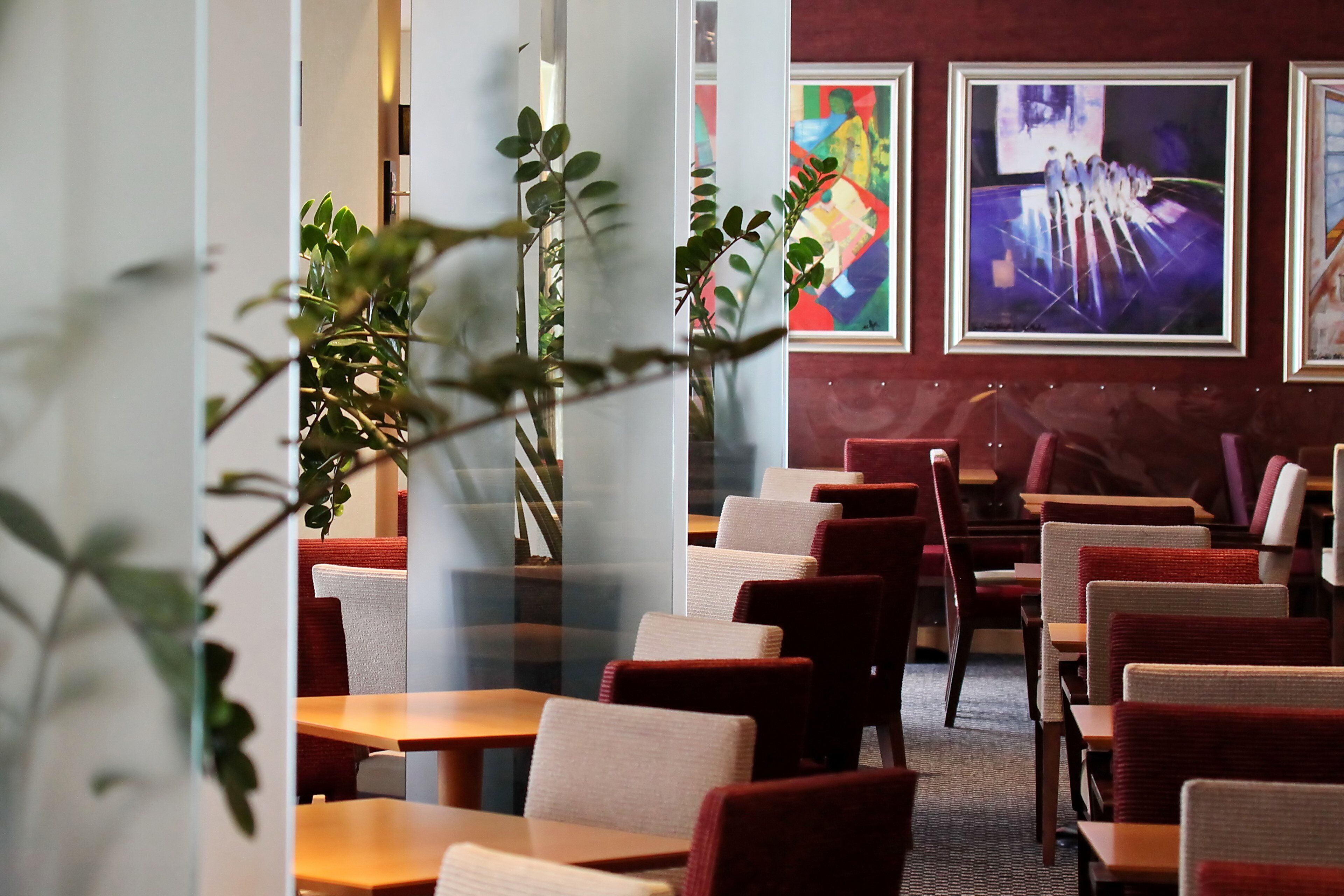 A restaurant interior with booths and tables, framed artwork on the walls, and potted plants.