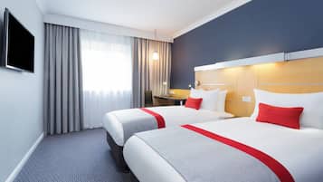 A hotel room with two beds, a flat-screen TV, a desk, and a window with curtains.