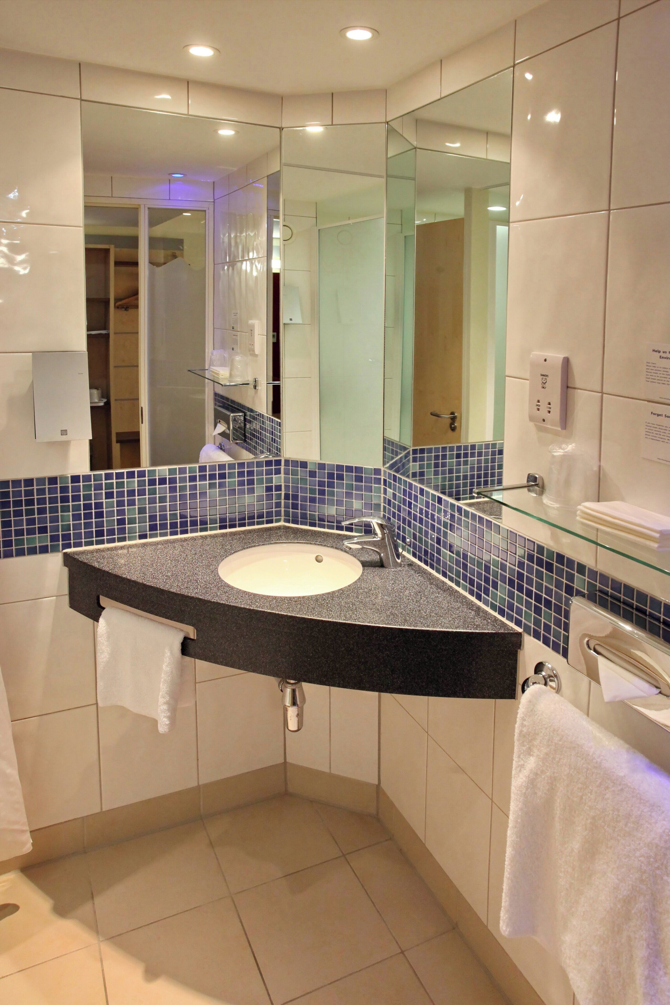 A modern bathroom with a curved sink, a glass shelf, and a large mirror.