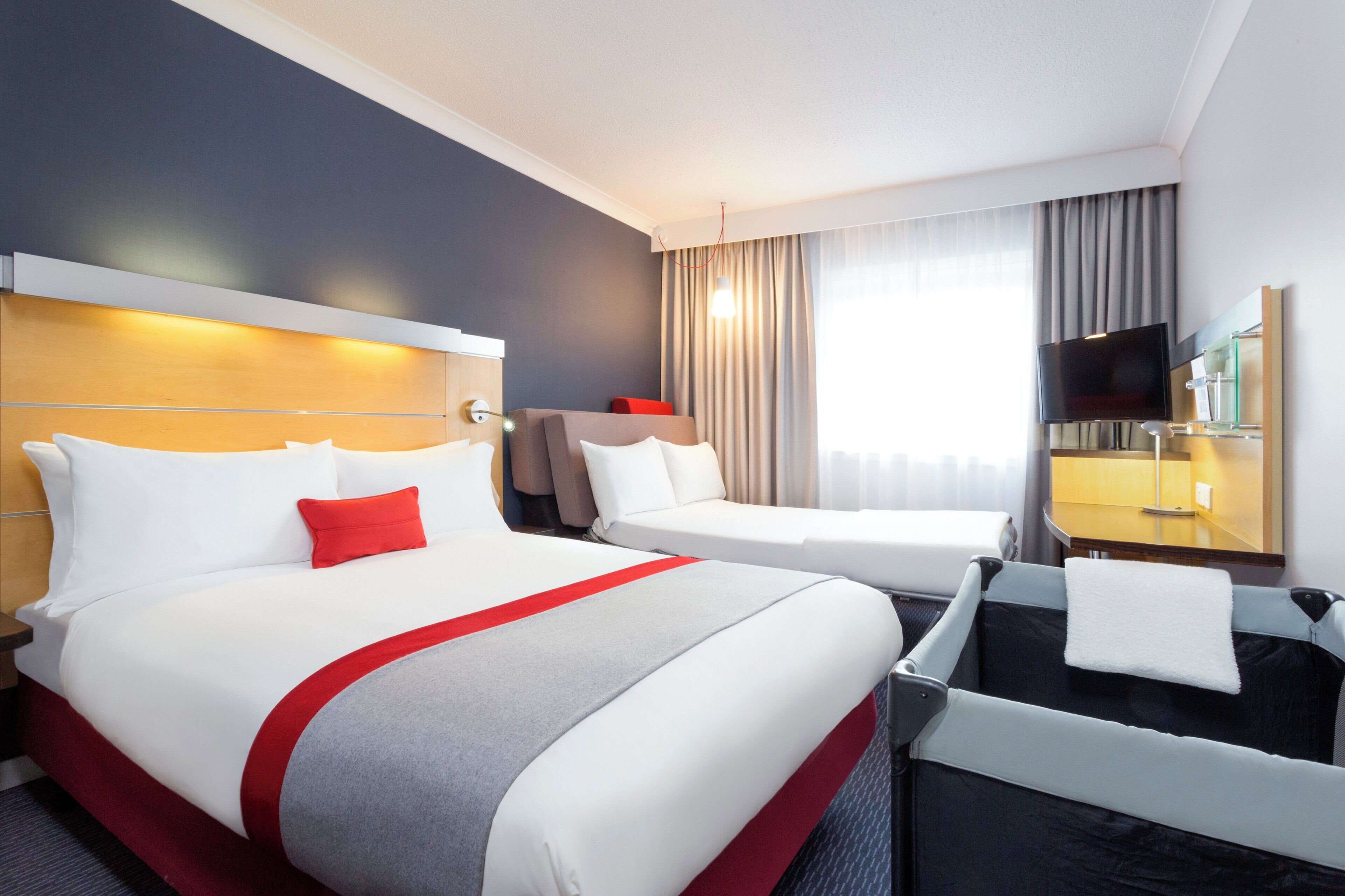 A hotel room with a bed, a desk, a chair, a TV, and a bathroom.