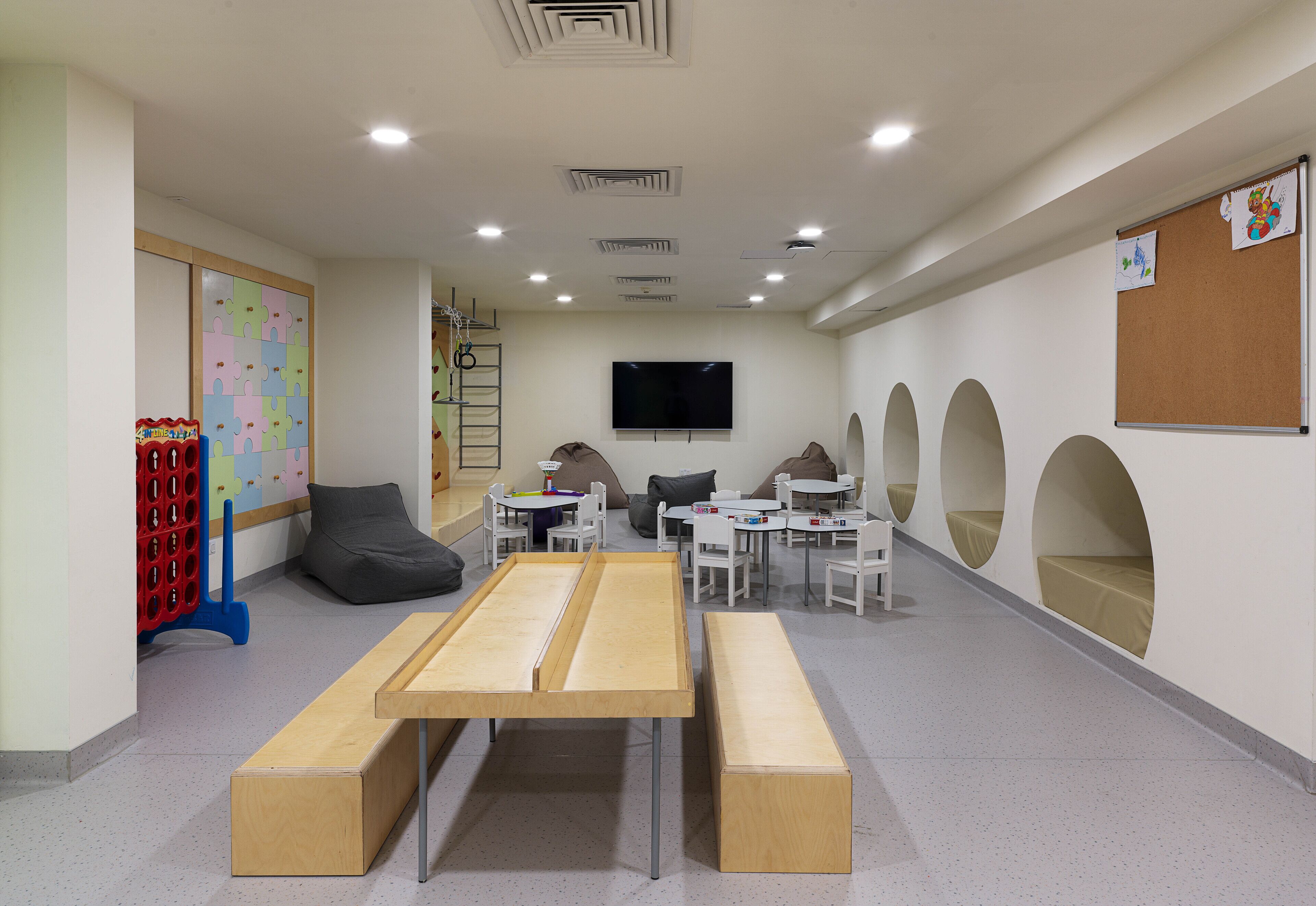 A children's playroom with a large wooden table, benches, and a TV on the wall.