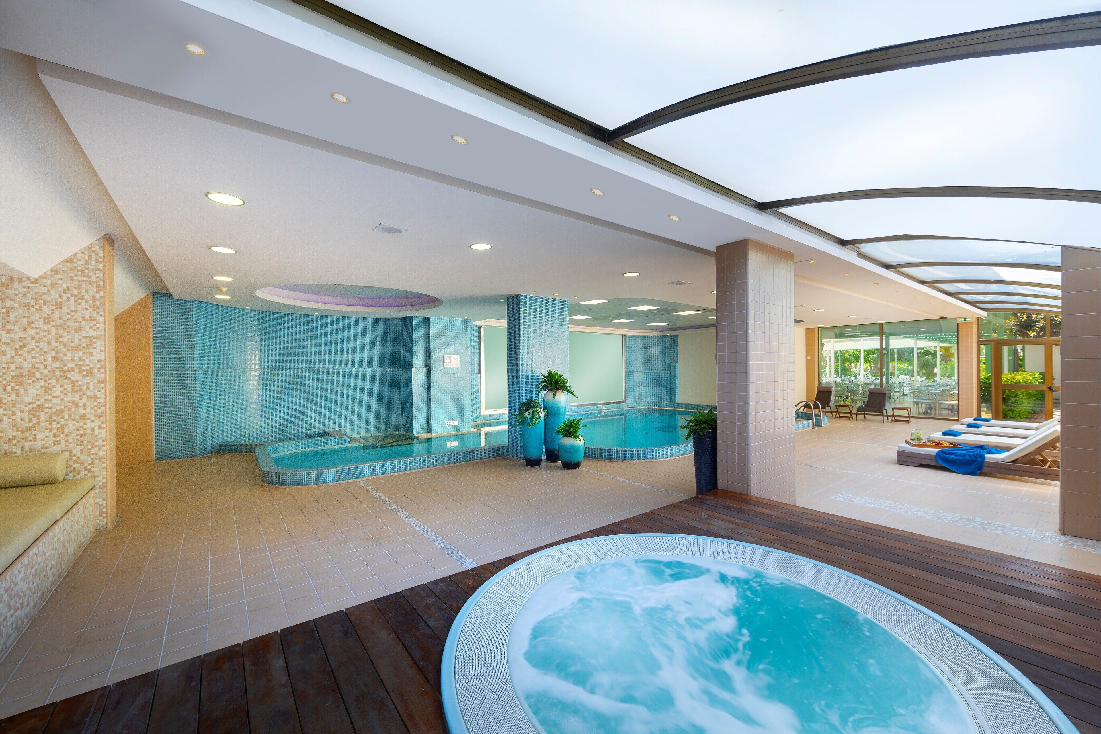 A modern indoor pool area with a hot tub, lounge chairs, and a seating area.