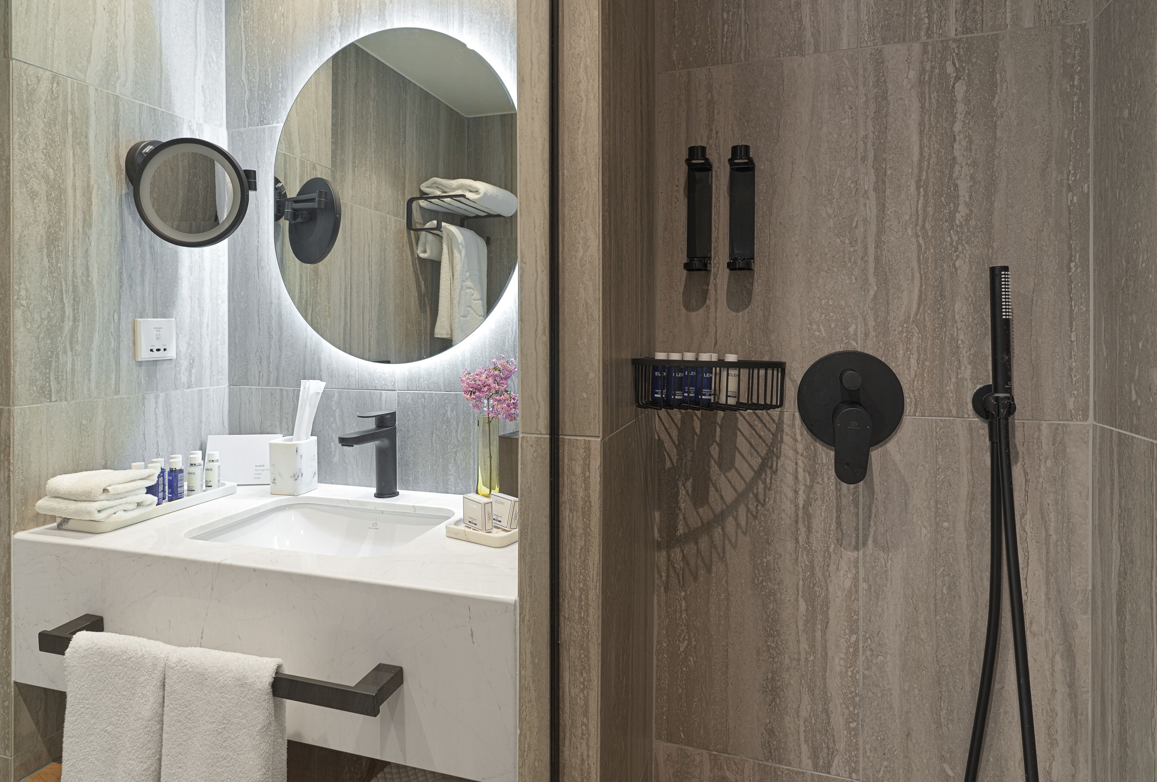 Un baño moderno con un espejo grande, un lavabo, un perchero para toallas y una zona de ducha con cabezal de ducha manual.