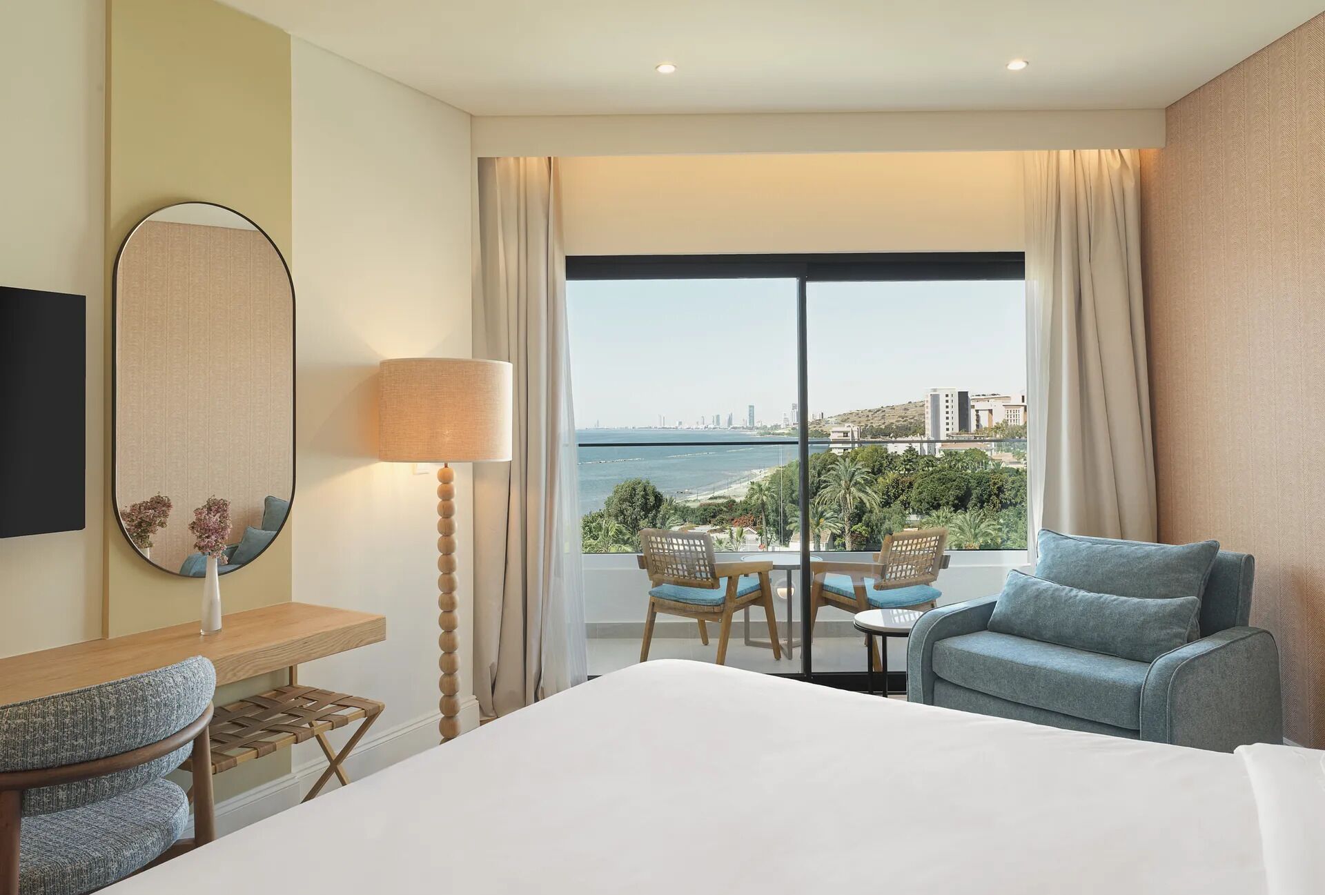 A hotel room with a bed, a desk, a chair, a table, and a view of the sea.