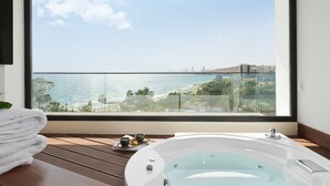Ein Balkon mit Blick auf das Meer und die Stadt, eine weiße Badewanne und ein Stapel weißer Handtücher.