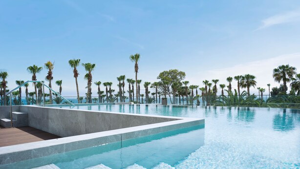 Ein unendlich wirkender Pool mit klarem, blauem Wasser, umgeben von Palmen und einem Holzboden.