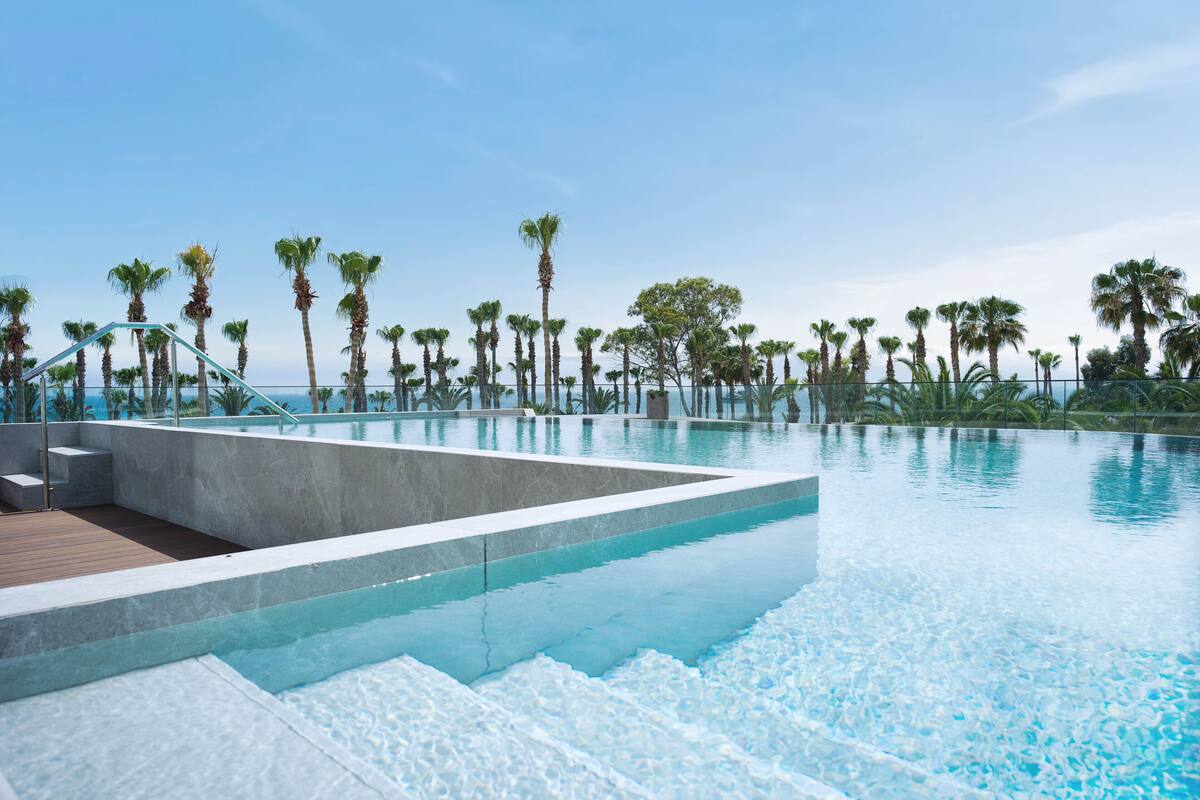 An infinity pool with clear blue water, surrounded by palm trees and a wooden deck.