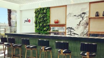 Een moderne bar met een groene wand, houten krukken en een decoratieve plank.