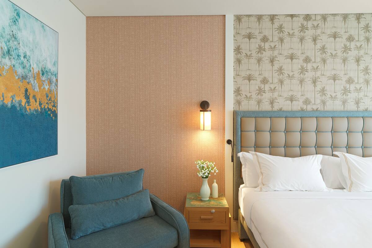 A hotel room with a bed, a nightstand with a lamp, a sofa, and a painting on the wall.