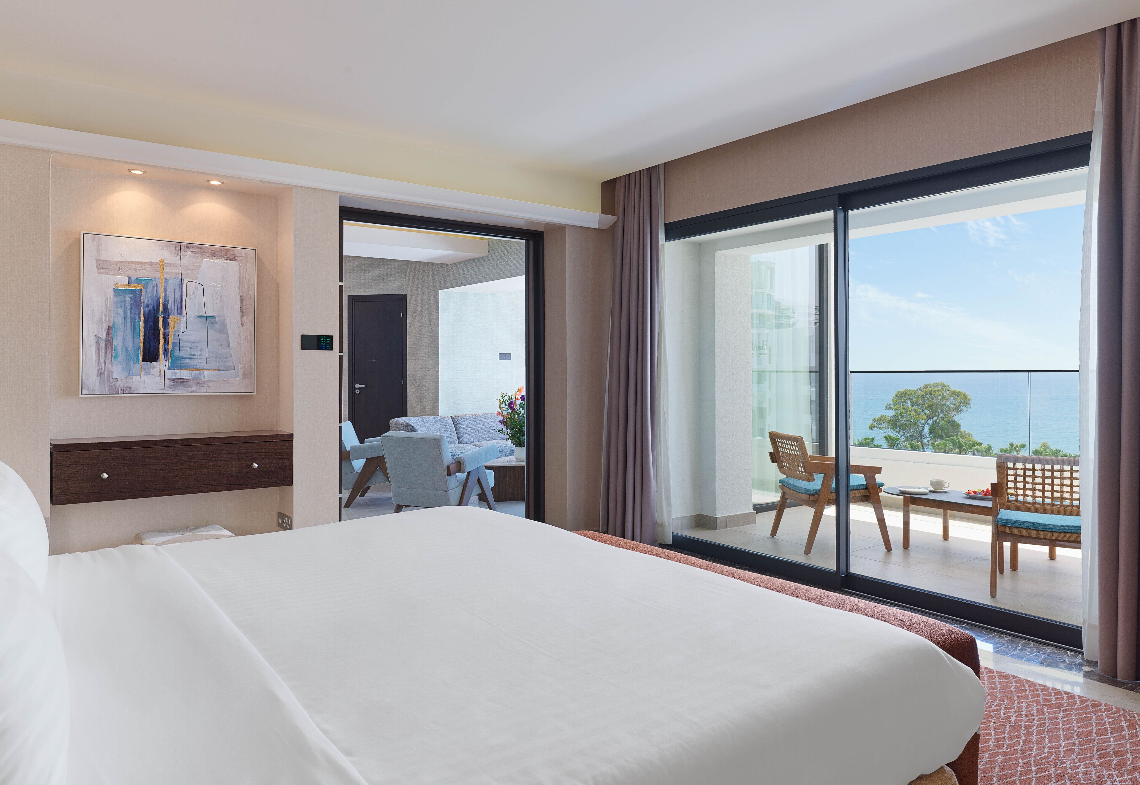 Une chambre d’hôtel avec un grand lit, un bureau et un balcon donnant sur la mer.