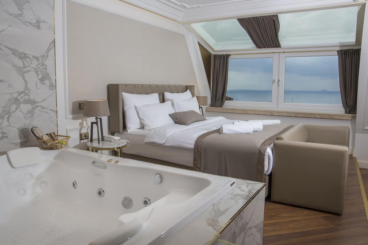 Una habitación de hotel moderna con una cama grande, una zona de estar, una bañera y vistas al mar.