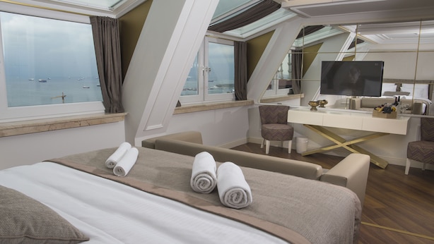 Una habitación de hotel moderna con cama, zona de estar, escritorio con televisor y vista al mar.