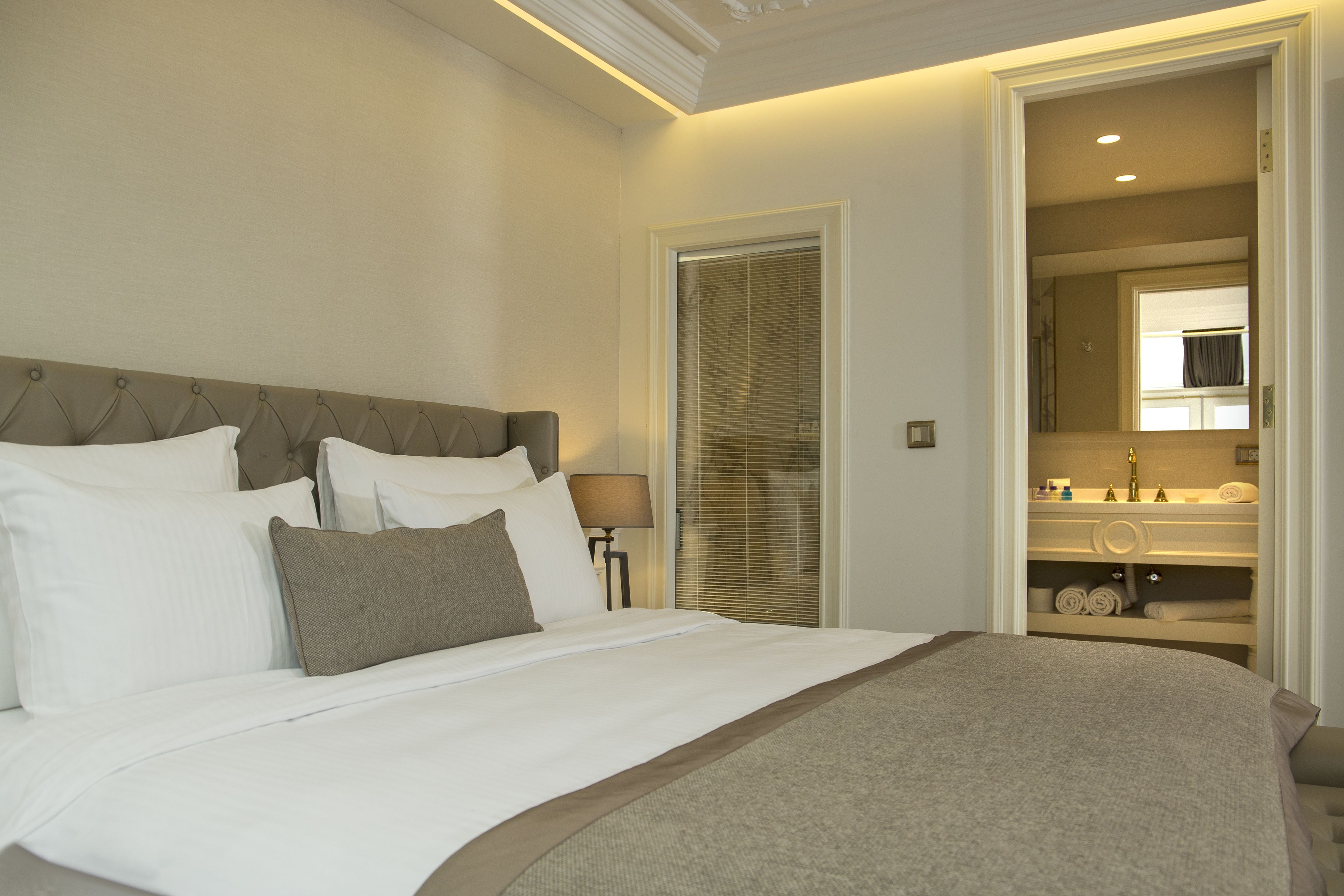 A neatly made bed with white and gray linens, a wooden headboard, and a bedside table with a lamp.