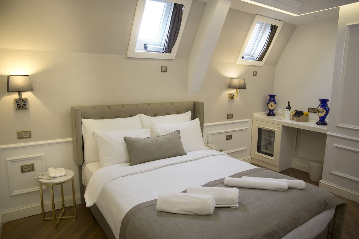 Un dormitorio ordenado con una cama grande, lámparas de noche, una mesita con un teléfono y un escritorio con un jarrón y una lámpara.