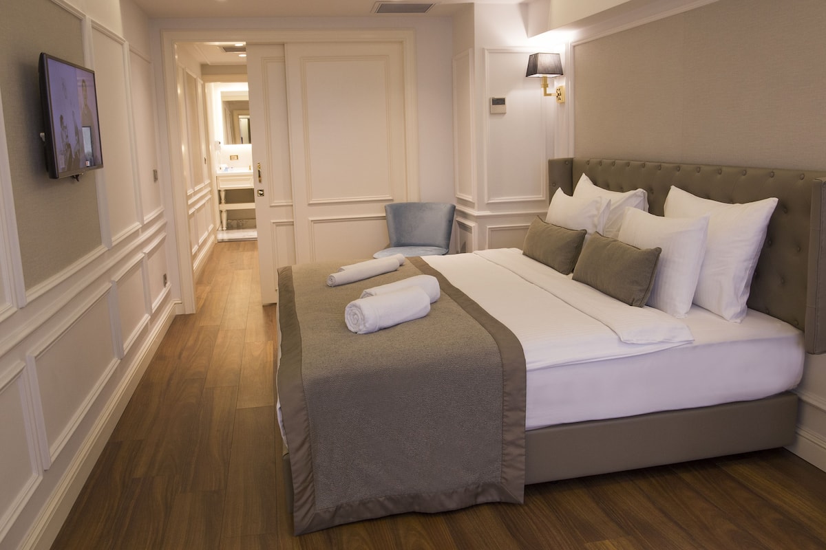 Una habitación de hotel con una cama grande, un televisor montado en la pared y una silla.