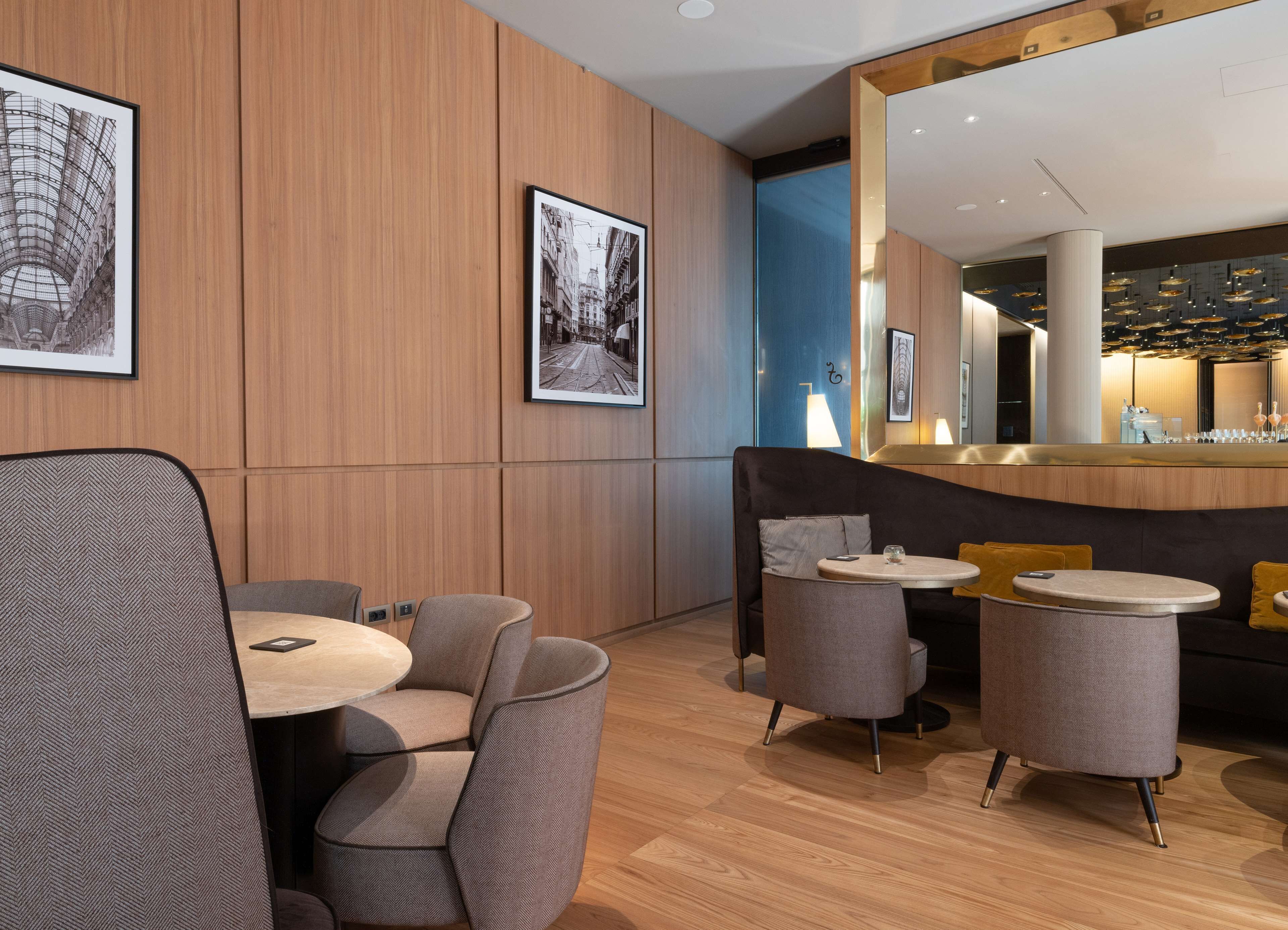 A modern interior with wooden panel walls, a bar area, and seating arrangements including round tables and cushioned chairs.