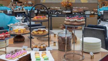 Buffet com diversos doces e pâtisseries, incluindo bolos, donuts e macarons, expostos em suportes e bandejas escalonados.