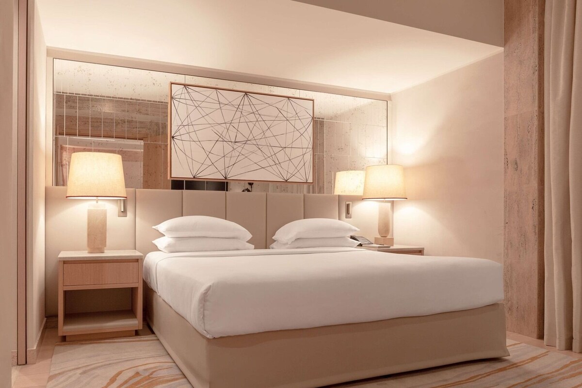 Una habitación de hotel moderna con una cama grande, dos lámparas de noche, una mesita de noche y un elemento decorativo en la pared.
