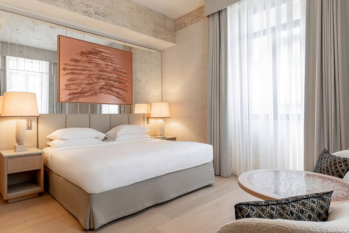 A hotel room with a large bed, two bedside lamps, a round coffee table, and a sofa.