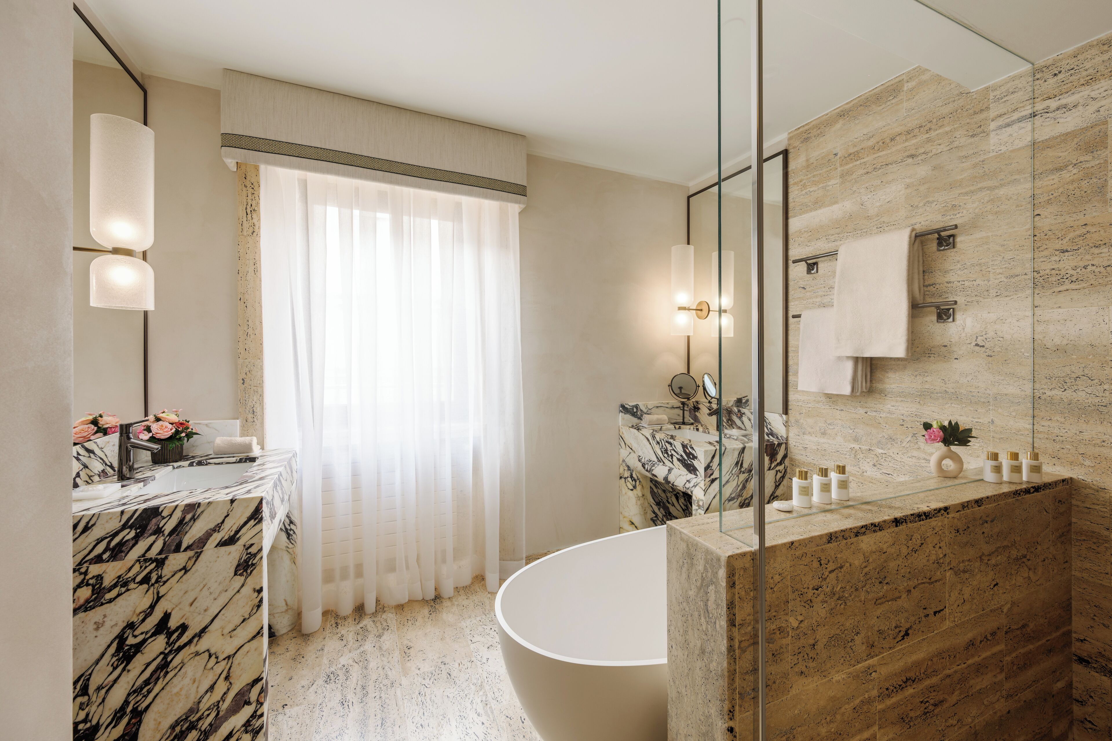 A modern bathroom with a marble vanity, a freestanding bathtub, and a glass shower enclosure.