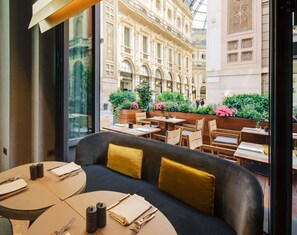 A restaurant with a view of a historic building, outdoor seating with tables and chairs, and a modern interior with a sofa and cushions. - Park Hyatt Milano (Milan)