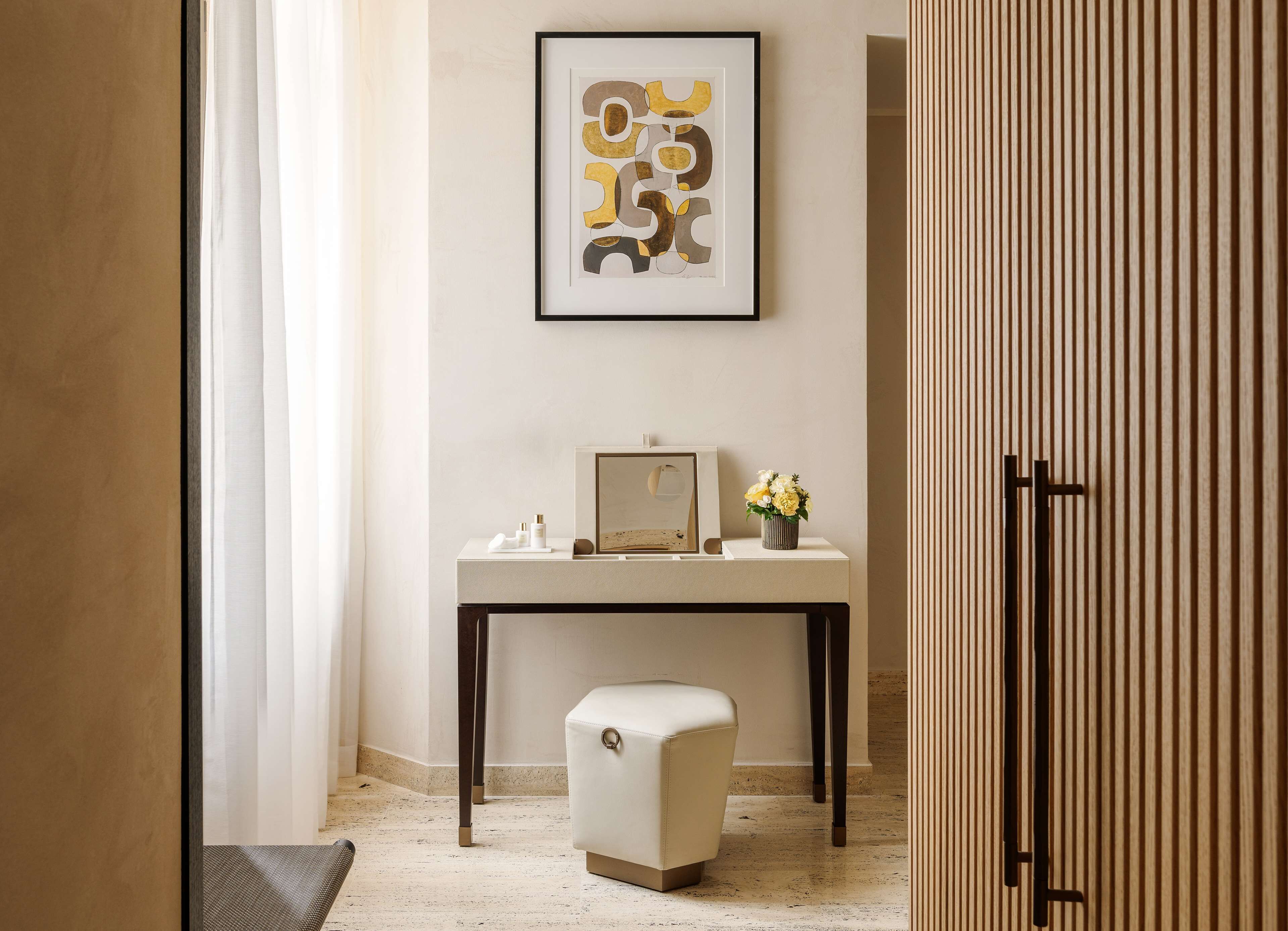A modern bathroom with a vanity, a framed abstract artwork, and a small stool.