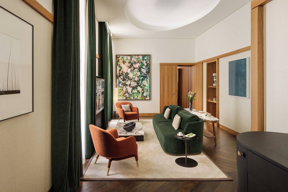 A modern living room with a green sofa, orange armchairs, a marble coffee table, and a wooden cabinet.