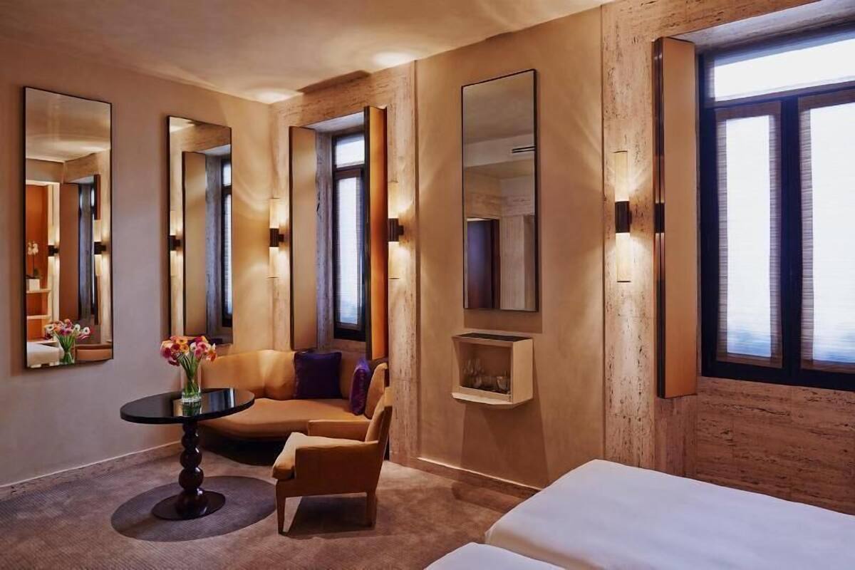 A hotel room with a sofa, a small table with a vase, a bed, and large mirrors on the walls.