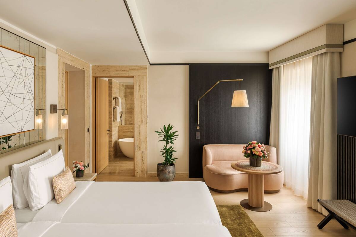 A modern hotel room with a large bed, a seating area with a round table, a potted plant, and a view of the bathroom.