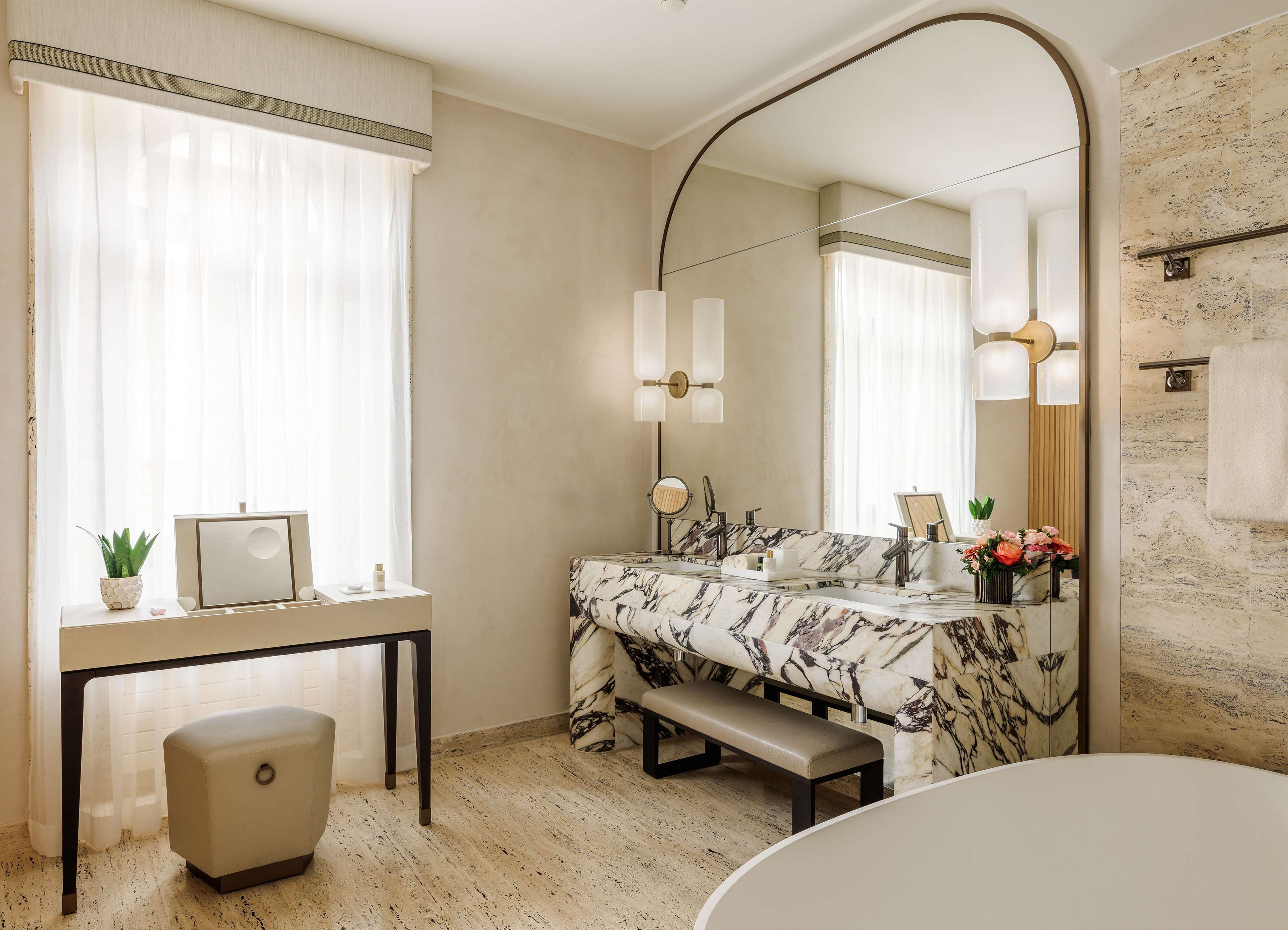 A bathroom with a marble vanity, a large mirror, a bench, and a bathtub.
