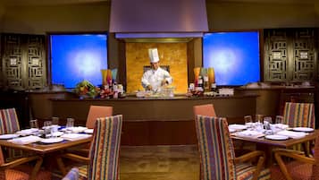 A chef preparing food at a counter in a restaurant with traditional decor and multiple tables set for dining.