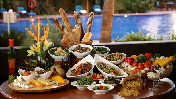 Ein reichhaltiges Buffet mit verschiedenen Speisen und Brot, mit Blick auf einen Pool.