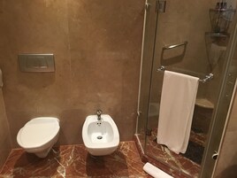 A bathroom with a bidet, a shower stall, and a marble floor.