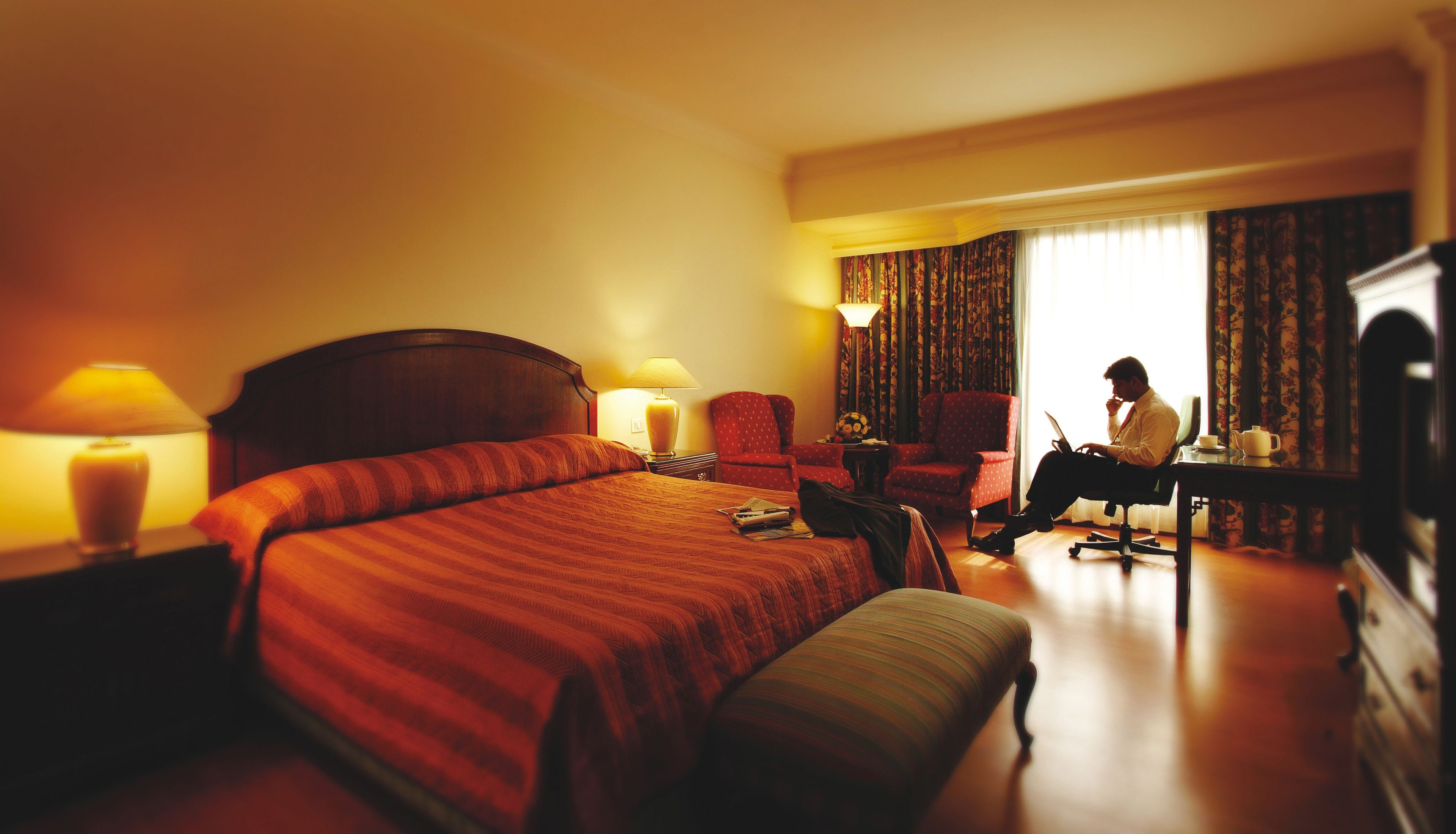 A hotel room with a large bed, a desk with a laptop, a chair, and a television.