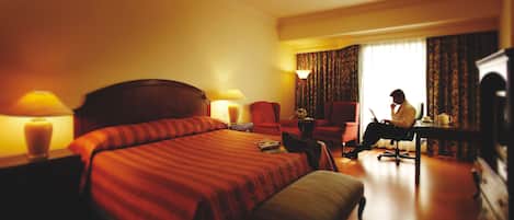 Una habitación de hotel con una cama grande, un escritorio con una computadora portátil, una silla y un televisor.