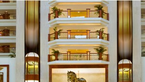 Eine mehrstöckige Hotelhalle mit einem zentralen Atrium, mehreren Balkonen und einer dekorativen Pferdestatue.