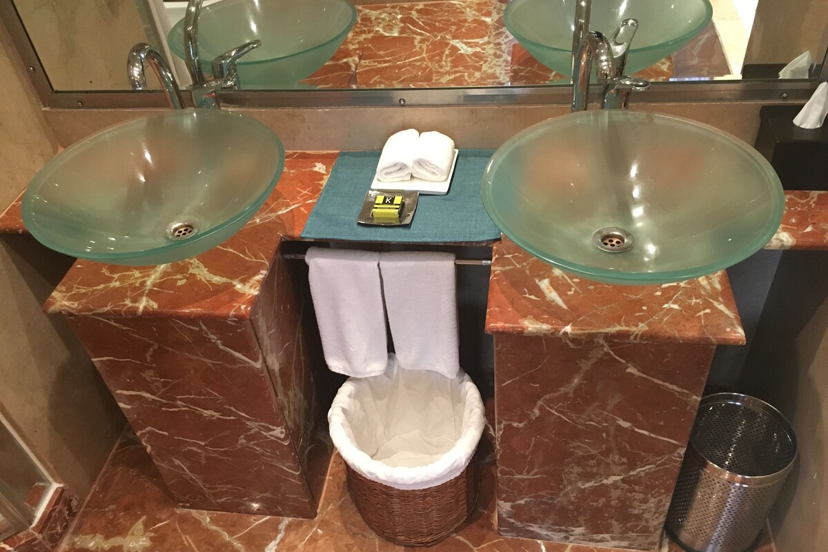 Un baño con dos lavamanos de vidrio, un perchero para toallas y un cesto de basura.