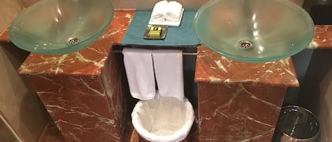 A bathroom with two glass sinks, a towel rack, and a waste basket.