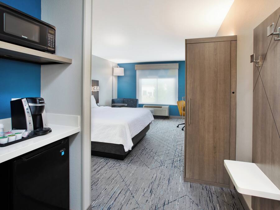Una habitación de hotel con una cama, un escritorio con cafetera, microondas y armario.