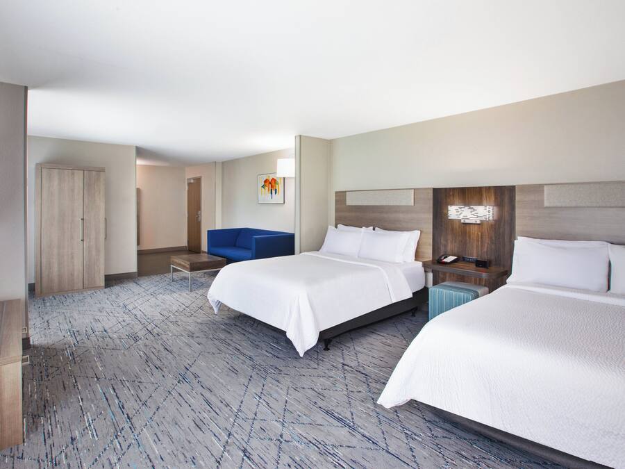 A hotel room with two beds, a desk, a chair, and a television.