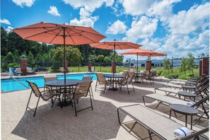 A poolside area with multiple tables and chairs, umbrellas, and a swimming pool.