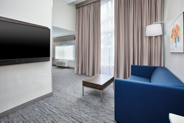 Une chambre d’hôtel équipée d’une télévision à écran plat, d’un canapé bleu, d’une petite table en bois et d’une grande fenêtre avec des rideaux.