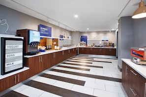 A modern breakfast area with a self-serve station, yogurt, eggs, and milk display, and a sign for express breakfast. - Holiday Inn Express & Suites W. Monroe by IHG (West Monroe)