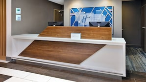 A hotel reception desk with a modern design, featuring a wooden accent and a blue geometric wall art piece. - Holiday Inn Express & Suites W. Monroe by IHG (West Monroe)