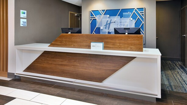 Un comptoir d’accueil d’hôtel au design moderne, agrémenté d’un élément décoratif en bois et d’une œuvre d’art murale aux motifs géométriques bleus.
